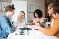 Group of young people sitting at the table and working together in office. Two pretty girls and two boys thoughtfully Royalty Free Stock Photo