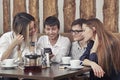 Group of young people from two couples of guys and girls have a tea time in the cafe and looking on the smartphone absorbedly Royalty Free Stock Photo