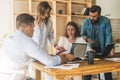 Group of young people work together. Man is using laptop, guy is holding smartphone. Girls flipping through magazine Royalty Free Stock Photo