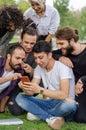 A group of young people are working in the park with mobile phones.They`re watching fun things on the phone