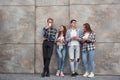 Group of young positive friends in casual clothes standing together against grey wall with cups of drink in hands Royalty Free Stock Photo