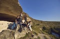 Group of young smiling tourists hikers having rest on natural rocks and enjoying green valley landscape