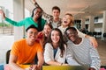 Group of young teenage students siting at library, using a laptop and looking at camera. Happy classmates studying and Royalty Free Stock Photo