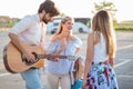 Group of young tourists having fun and playing guitar in a parking lot, waiting for transport