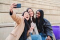 Group of young woman having fun doing a selfie with smartphone. Three multiracial happy girls amiling taking a photo