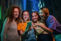 Group of young women having fun sharing media on the social media with a cellphone at night. Three girls looking to the Royalty Free Stock Photo