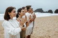 Group of young women and men meditating during their morning practice on the beach on ocean shore, free space Royalty Free Stock Photo