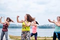 A group of young women, wearing colorful sports outfits, doing zumba exercises outside by city lake. Dancing training to loose Royalty Free Stock Photo