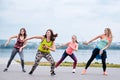 A group of young women, wearing colorful sports outfits, doing zumba exercises outside by city lake. Dancing training to loose Royalty Free Stock Photo