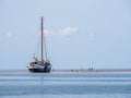 Group of youngsters on sand flat and flat-bottom sailboat at low