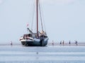 Group of youngsters on sand flat and flat-bottom sailboat at low Royalty Free Stock Photo