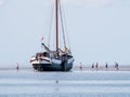 Group of youngsters on sand flat and flat-bottom sailboat at low