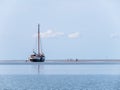 Group of youngsters on sand flat and flat-bottom sailboat at low