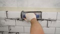 Grouting tiles with rubber trowel man hand. Professional worker gluing decorative tile on wall. Grouting white tiles. Royalty Free Stock Photo