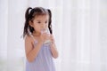 A growing Asian girl stands in her bedroom and enjoys a delicious breakfast of fresh milk