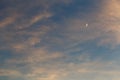 A growing moon in the blue sky among the clouds illuminated by the sun at sunset