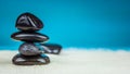 Growing piled up of four black pebbles on bright sand with blue background Royalty Free Stock Photo