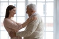 Grownup granddaughter visited elderly grandfather hugs him standing indoors