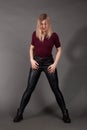 Growth Portrait of the blonde in the red sweater with short sleeves, leather trousers and boots. Studio shot on dark gray Royalty Free Stock Photo