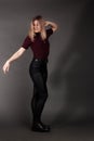 Growth Portrait of the blonde in the red sweater with short sleeves, leather trousers and boots. Studio shot on dark gray Royalty Free Stock Photo