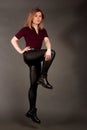 Growth Portrait of the blonde in the red sweater with short sleeves, leather trousers and boots. Studio shot on dark gray Royalty Free Stock Photo