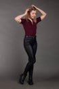 Growth Portrait of the blonde in the red sweater with short sleeves, leather trousers and boots. Studio shot on dark gray Royalty Free Stock Photo