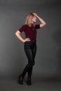 Growth Portrait of the blonde in the red sweater with short sleeves, leather trousers and boots. Studio shot on dark gray Royalty Free Stock Photo