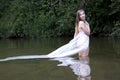 Growth portrait of a girl in a white dress standing in river