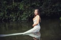 Growth portrait of a girl in a white dress standing in river