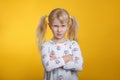 Grumpy angry Caucasian blonde girl with blue eyes in white dress posing in studio on yellow background