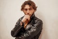 Young and and thoughtful male model with curly hair posing in a studio wearing leather jacket Royalty Free Stock Photo