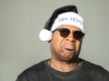 Grumpy middle aged African American man wearing a hat saying Bah Humbug against a solid background