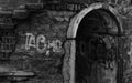 Grunge dungeon entrance in a wall with antique masonry with obscene writing on the wall