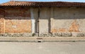 Grunge wall made with bricks and old peeled paint. Terracotta tiled roof , sidewalk and asphalt road in front. Royalty Free Stock Photo