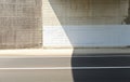 Grunge white and gray concrete wall of an underpass divided in two by the shadow of the bridge. Two lane road in front.