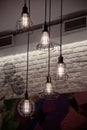 Grungy wire lampshades hanged on cable from ceiling with brick wall background. Lamps with shiny filaments inside retro lightbulbs
