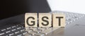 GST abbreviation stands for written on a wooden cube on laptop