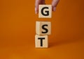 GST - Goods and Services Tax symbol. Concept word GST on wooden cubes. Businessman hand. Beautiful orange background. Business and Royalty Free Stock Photo