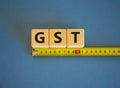 GST, goods and services tax symbol. The word GST, goods and services tax on cubes arranged behind the ruler on beautiful blue