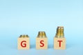 GST letters on wooden blocks in blue background increasing stack of coins. Increase on goods and services tax Royalty Free Stock Photo