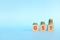 GST letters on wooden blocks in blue background increasing stack of coins. Increase on goods and services tax Royalty Free Stock Photo