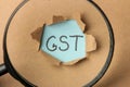 GST word and torn paper and magnifier. Taxes on the background of craft paper. top view Royalty Free Stock Photo