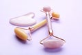 Gua sha stone and different face rollers on violet background