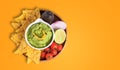 Guacamole bowl with nachos and ingredients on orange background with copy space