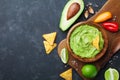 Guacamole dip with avocado, lime and nachos on black table top view. Copy space.Traditional mexican food.