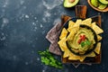 Guacamole. Traditional latinamerican Mexican dip sauce in a black bowl with avocado and ingredients and corn nachos. Avocado