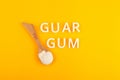 Guar gum powder or guaran in wooden spoon on yellow background. Food additive E412. Inscription GUAR GUM. Extract of seed