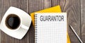 GUARANTOR text on the notebook with coffee on wooden background