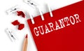 GUARANTOR text on red paper with office tools on white background