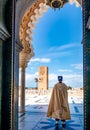 Guard soldier in national costume at the entrance of Mausoleum of Mohammed V and square with Hassan tower in Rabat on sunny day.